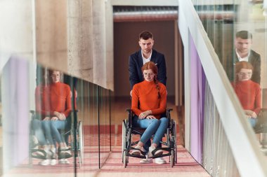 Bir şirket müdürü, iş arkadaşına tekerlekli sandalyede yardım ederek, farklı meslekdaşlarından oluşan ekiple birlikte çalıştıkları başlangıç ofislerine kadar rehberlik eder.