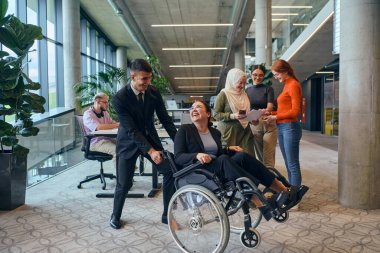 A diverse group of business colleagues is having fun with their wheelchair-using colleague, demonstrating their attention and inclusivity in the workplace.  clipart
