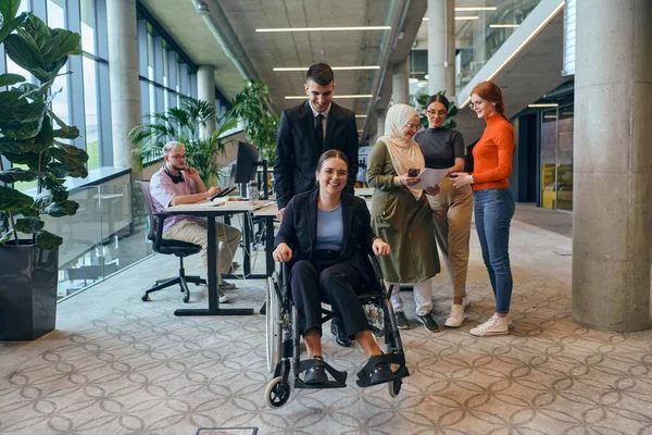 多様なビジネス同僚が車椅子を使った同僚と楽しく過ごし 職場での注目と寛容さを示しています — ストック写真