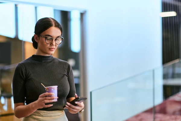 活気あふれる現代オフィスで メガネをかけたビジネスマンが仕事をジャグリングし コーヒーを飲み スマートフォンを使用して 現代の企業生活のダイナミックで多面的な性質を象徴しています — ストック写真