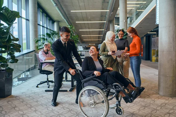 stock image A diverse group of business colleagues is having fun with their wheelchair-using colleague, demonstrating their attention and inclusivity in the workplace. 