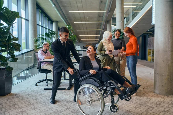 stock image A diverse group of business colleagues is having fun with their wheelchair-using colleague, demonstrating their attention and inclusivity in the workplace. 