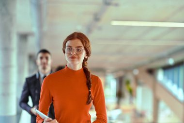 Modern bir girişim şirketinin dinamik ortamında, yönetici genç iş arkadaşı ile yürürken bir tartışma içine girer, işbirliği ve yenilik ruhunu yansıtır.