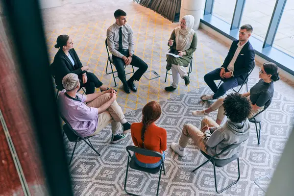 Top view of a diverse group of young business entrepreneurs gathered in a circle for a meeting, discussing corporate challenges and innovative solutions within the modern confines of a large