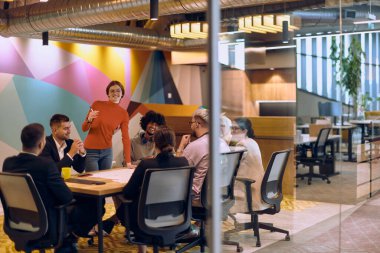 Modern cam bir ofiste çeşitli uzmanlardan oluşan bir ekip, dikkatle bir meslektaşlarını dinliyor, işbirliği ve yenilikleri teşvik ediyorlar.