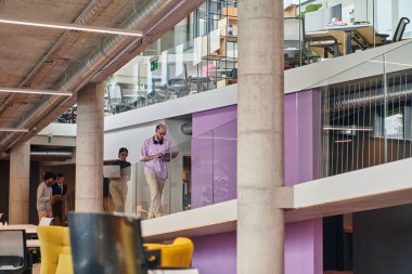 Modern kurumsal dünyada, çeşitli geçmiş ve kültürleri temsil eden çeşitli iş adamları grubu, modern bir girişim ofisinin koridorunda yürür,