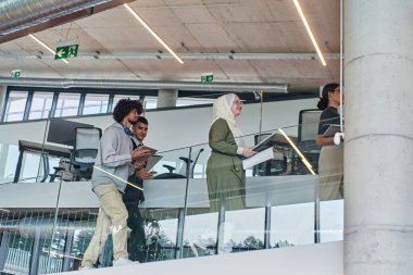 Modern kurumsal dünyada, çeşitli geçmiş ve kültürleri temsil eden çeşitli iş adamları grubu, modern bir girişim ofisinin koridorunda yürür,