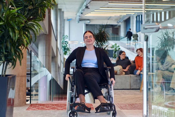 近代的なオフィスでは 車椅子の若い実業家が彼女の支持する同僚に囲まれ 職場での寛大さと多様性の精神を体現しています — ストック写真