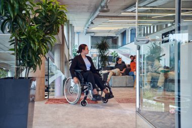 Modern bir ofiste, tekerlekli sandalyedeki genç bir iş kadını, iş hayatına dahil olma ve çeşitlilik ruhunu somutlaştıran destekleyici meslektaşlarıyla çevrilidir.. 