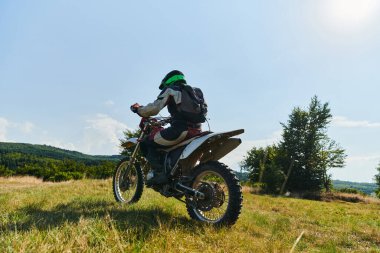 Profesyonel teçhizatla donatılmış bir motosikletli tehlikeli çayırlarda motokros sürüyor, yaklaşan bir yarışma için hazırlanıyor.