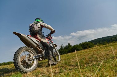 Profesyonel teçhizatla donatılmış bir motosikletli tehlikeli çayırlarda motokros sürüyor, yaklaşan bir yarışma için hazırlanıyor.