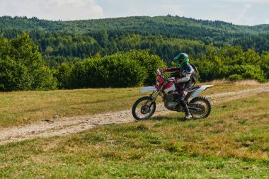 Profesyonel teçhizatla donatılmış bir motosikletli tehlikeli çayırlarda motokros sürüyor, yaklaşan bir yarışma için hazırlanıyor.