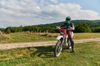 Profesyonel teçhizatla donatılmış bir motosikletli tehlikeli çayırlarda motokros sürüyor, yaklaşan bir yarışma için hazırlanıyor.