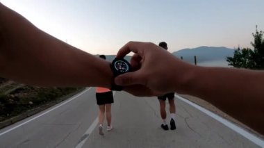 Sporcu egzersizden önce akıllı saat kuruyor. Panoramik bir kırsal yolda birlikte koşan çok ırklı bir grup sporcu. Çeşitli koşu takımları sabah antrenmanında. POV göğüs munt eylemi