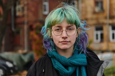 Evinin önündeki parkta çekilen çarpıcı mavi saçlı, büyüleyici bir genç kız portresi karizmatik ve stil sahibi kişiliğini doğal bir açık hava karakterine karşı sergiliyor.