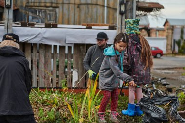 Modern bir aile babası ve çocuklar, gelecek tatil sezonuna hazırlanmak için bahçelerini çiçeklerle süslemek için birlikte çalışıyorlar.