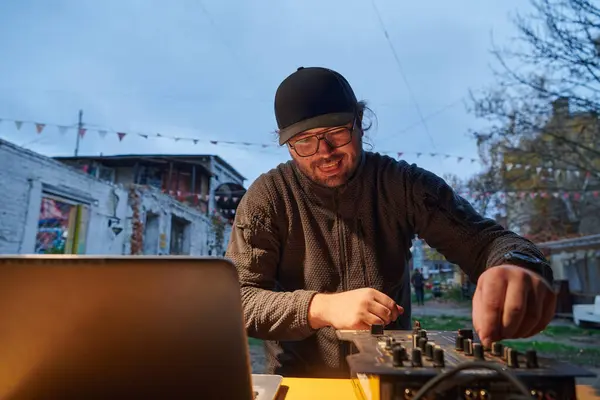 A young man is entertaining a group of friends in the backyard of his house, becoming their DJ and playing music in a casual outdoor gathering.