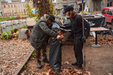 Baba-kız çiftler bahçede birlikte çalışıp dökülen yaprakları toplar ve gevrek bir sonbahar gününde bir poşeti doldururlar.