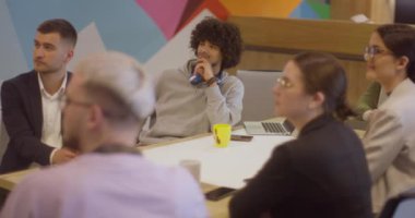 Modern cam bir ofiste çeşitli uzmanlardan oluşan bir ekip, dikkatle bir meslektaşlarını dinliyor, işbirliği ve yenilikleri teşvik ediyorlar..