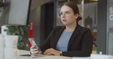  Modern bir ofiste akıllı telefon kullanan tekerlekli sandalyede hayal kırıklığına uğramış bir kadın, karşılaştığı zorluklara rağmen iş yerinde ulaşılabilirlik ve kapsayıcılığın önemini vurguluyor.. 