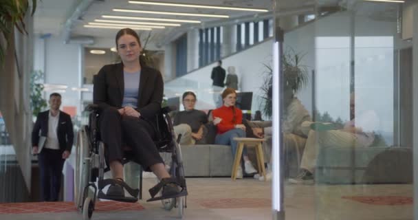 彼女の後ろで話し合っている同僚と現代の会社の車椅子のビジネスマンは 寛大さ 多様性 共同議論を重視する職場を象徴しています — ストック動画