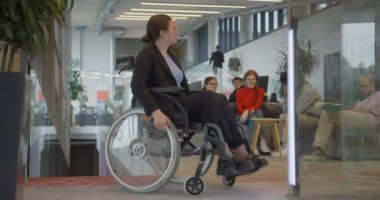 Modern bir şirkette iş arkadaşlarıyla birlikte tekerlekli sandalyedeki bir iş kadını, iş yerinin kapsayıcılığa, çeşitliliğe ve işbirliğine değer verdiğini sembolize ediyor..