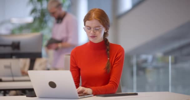 現代的なスタートアップオフィスでは ノートパソコンに座ってオレンジ色の髪を持つプロのビジネスマンが 現代のワークスペースで革新性と生産性を象徴しています — ストック動画