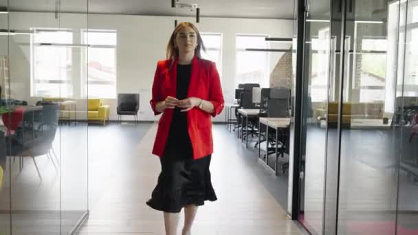 一位穿着鲜红色服装的自信的女商人优雅地在现代创业空间的走廊中穿行 展现出时尚和专业精神 — 图库视频影像