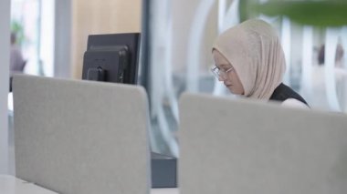 Modern bir ofiste, başörtüsü takan Müslüman bir girişimci güvenli ve gayretli bir şekilde bilgisayarında oturur, kararlılığı, yaratıcılığı ve iş dünyasının güçlendirilmesini somutlaştırır.. 