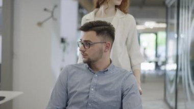 Genç iş arkadaşları, işbirlikçi iş arkadaşları, aralarında tekerlekli sandalyedeki bir kişinin de bulunduğu, modern cam ofis koridorunun yanından geçerek, çeşitliliği, takım çalışmasını ve güçlendirmeyi resmediyorlar.