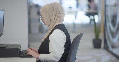 Modern bir ofiste, başörtüsü takan Müslüman bir girişimci güvenli ve gayretli bir şekilde bilgisayarında oturur, kararlılığı, yaratıcılığı ve iş dünyasının güçlendirilmesini somutlaştırır.. 