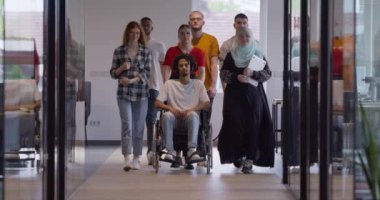 Genç iş adamlarından oluşan çeşitli bir grup, modern bir girişim olan cam kaplı bir ofiste, tekerlekli sandalyedeki bir kişi, bir Afrikalı Amerikalı genç adam ve bir tesettür ile bir araya geliyor.
