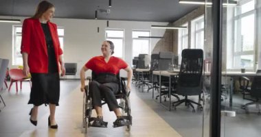 Kendi durumundan dolayı tekerlekli sandalye kullanan genç bir girişimci, modern, kapsayıcı ofislerde geziniyor, işyerinde azim ve güç gösterisi yapıyor.