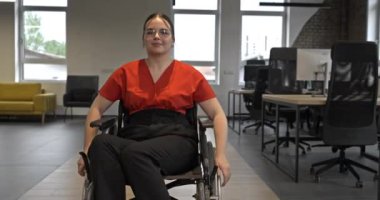 Kendi durumundan dolayı tekerlekli sandalye kullanan genç bir girişimci, modern, kapsayıcı ofislerde geziniyor, işyerinde azim ve güç gösterisi yapıyor.