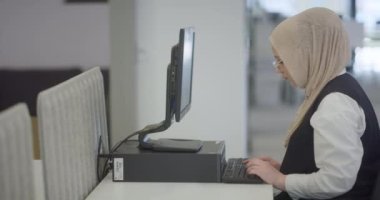 Modern bir ofiste, başörtüsü takan Müslüman bir girişimci güvenli ve gayretli bir şekilde bilgisayarında oturur, kararlılığı, yaratıcılığı ve iş dünyasının güçlendirilmesini somutlaştırır.. 
