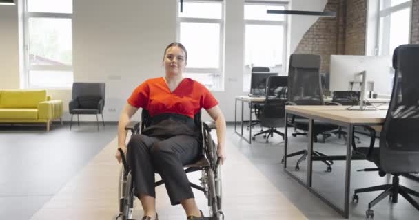 若い女性起業家は 彼女の状態のために車椅子を使用して 近代的で包括的なオフィスをナビゲートし 職場での決意とエンパワーメントを示しています — ストック動画