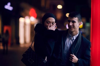 Mutlu çok kültürlü iş çifti gece vakti bir kuyumcunun vitrinine yakın bir şehir sokağında birlikte yürüyorlar. Başarılı Arap işadamı ve Avrupalı Müslüman kadın.