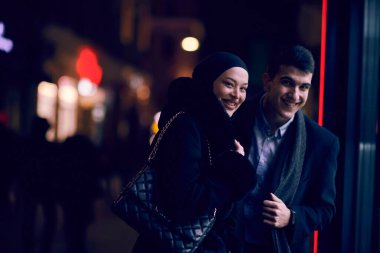 Mutlu çok kültürlü iş çifti gece vakti bir kuyumcunun vitrinine yakın bir şehir sokağında birlikte yürüyorlar. Başarılı Arap işadamı ve Avrupalı Müslüman kadın.