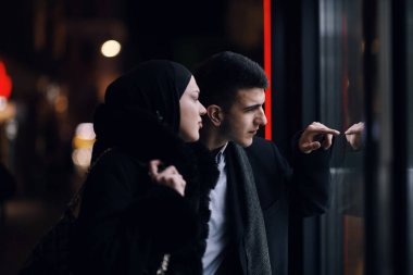 Mutlu çok kültürlü iş çifti gece vakti bir kuyumcunun vitrinine yakın bir şehir sokağında birlikte yürüyorlar. Başarılı Arap işadamı ve Avrupalı Müslüman kadın.