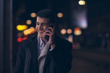 Gülümseyen Meedle Eastern adamı modern ofis binasının yakınındaki caddede yürüyor, serbest çalışan işadamı geceleri işlek şehir caddesinde elinde cep telefonuyla diğer tarafa bakıyor.