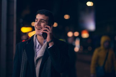 Gülümseyen Meedle Eastern adamı modern ofis binasının yakınındaki caddede yürüyor, serbest çalışan işadamı geceleri işlek şehir caddesinde elinde cep telefonuyla diğer tarafa bakıyor.