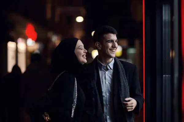 ハッピーな多文化ビジネスカップルは ジュエリーショッピングストアの窓の近くで夜に都市街の通りで屋外を歩いています 成功したアラブのビジネスマンとヨーロッパのムスリム女性 — ストック写真