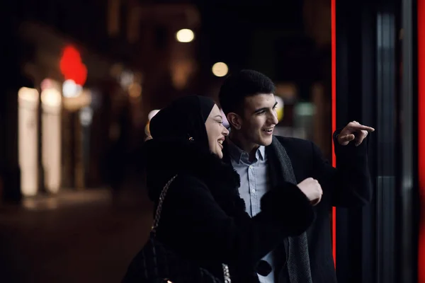 ハッピーな多文化ビジネスカップルは ジュエリーショッピングストアの窓の近くで夜に都市街の通りで屋外を歩いています 成功したアラブのビジネスマンとヨーロッパのムスリム女性 — ストック写真