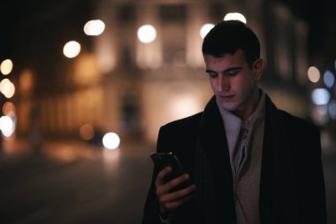 Gülümseyen Meedle Eastern adamı modern ofis binasının yakınındaki caddede yürüyor, serbest çalışan işadamı geceleri işlek şehir caddesinde elinde cep telefonuyla diğer tarafa bakıyor.