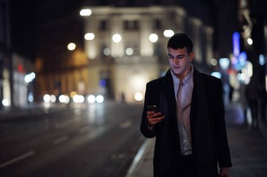 Gülümseyen Meedle Eastern adamı modern ofis binasının yakınındaki caddede yürüyor, serbest çalışan işadamı geceleri işlek şehir caddesinde elinde cep telefonuyla diğer tarafa bakıyor.