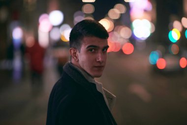 Gülümseyen Meedle Eastern adamı modern ofis binasının yakınındaki caddede yürüyor, serbest çalışan işadamı geceleri işlek şehir caddesinde elinde cep telefonuyla diğer tarafa bakıyor.