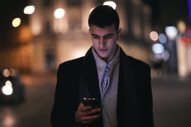 Gülümseyen Meedle Eastern adamı modern ofis binasının yakınındaki caddede yürüyor, serbest çalışan işadamı geceleri işlek şehir caddesinde elinde cep telefonuyla diğer tarafa bakıyor.