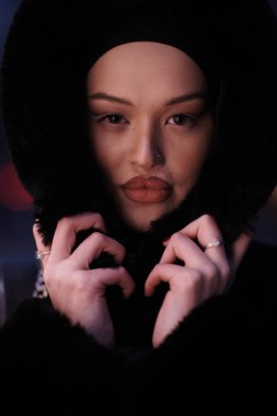 Soğuk bir kış gecesinde şehir caddesinde yürüyen Müslüman bir kadın arka planda Bokeh şehir ışıklarıyla tesettüre girmiş.