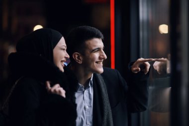 Mutlu çok kültürlü iş çifti gece vakti bir kuyumcunun vitrinine yakın bir şehir sokağında birlikte yürüyorlar. Başarılı Arap işadamı ve Avrupalı Müslüman kadın.