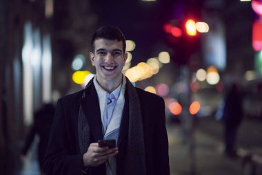 Gülümseyen Meedle Eastern adamı modern ofis binasının yakınındaki caddede yürüyor, serbest çalışan işadamı geceleri işlek şehir caddesinde elinde cep telefonuyla diğer tarafa bakıyor.